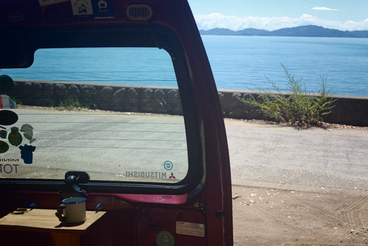 海沿いに停めた車内で、ホーローマグとコーヒーを楽しむ様子